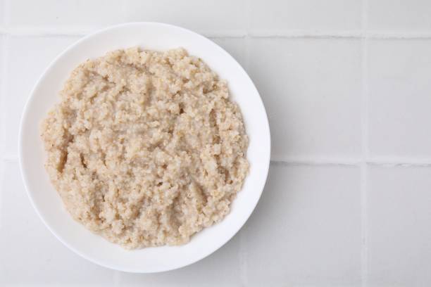 istock Delicious barley porridge in bowl on white tiled table, top view. Space for text 2180128506