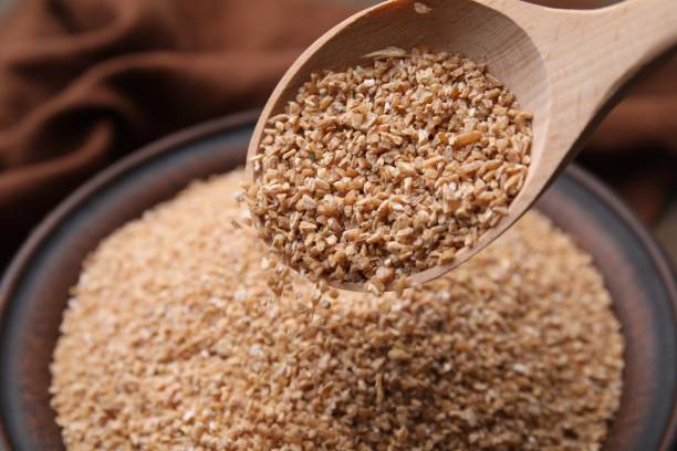 istock Pouring dry wheat groats from spoon into bowl, closeup 2180128729