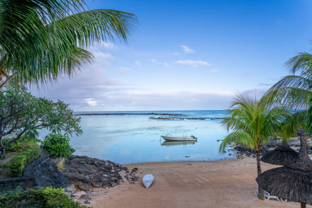 A small boat anchored in a calm turquoise lagoon, surrounded by a pristine white sandy beach and palm trees. The idyllic scene is captured at Ile aux Cerfs, Mauritius. Mauritius, Africa.