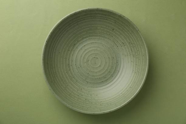 Beautiful ceramic bowl on green background, top view