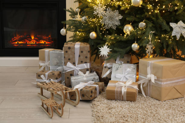istock Many gift boxes and decorative sleighs under beautiful Christmas tree near fireplace at home 2180133388