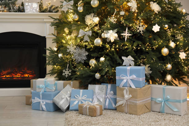 istock Many gift boxes under beautiful Christmas tree near fireplace at home 2180133459