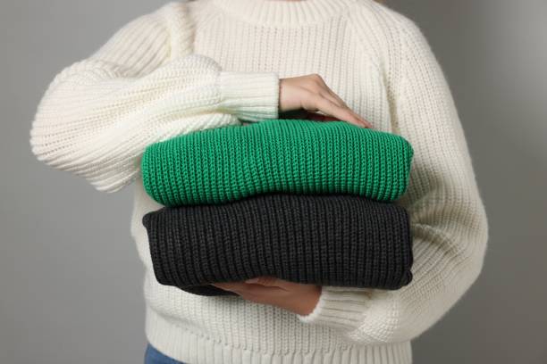 istock Woman with stack of knitted sweaters on grey background, closeup 2180133466