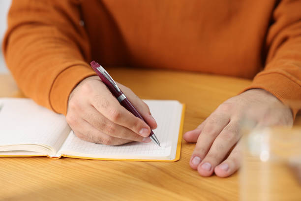 istock Young man writing in notebook at wooden table, closeup 2180140176