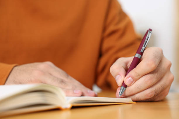 istock Young man writing in notebook at wooden table, closeup 2180140250