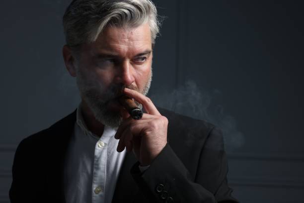 istock Handsome bearded man smoking cigar against dark grey background. Space for text 2180140292