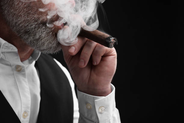 istock Bearded man smoking cigar against black background, closeup. Space for text 2180140347