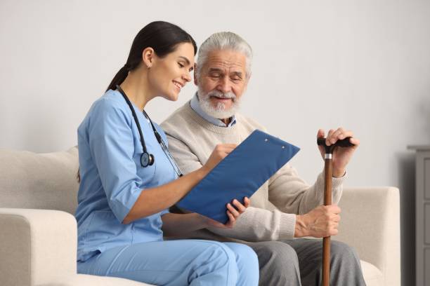 istock Smiling nurse with clipboard assisting elderly patient on sofa in hospital 2180143701
