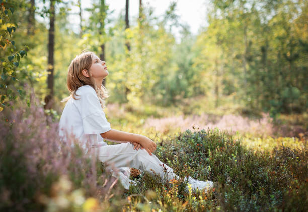 istock A young child sitting quietly in a serene forest, surrounded by vibrant greenery during a sunny afternoon 2180147398