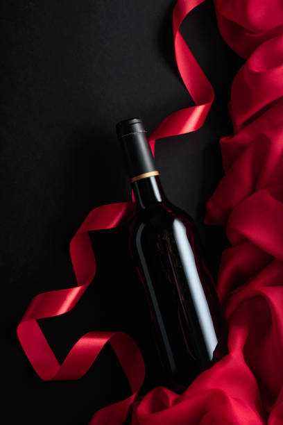 istock Bottle of red wine with red satin on a black background. 2180157803