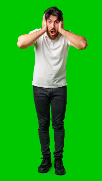 istock A man with a surprised expression holds his face while against a vibrant green background 2180165538