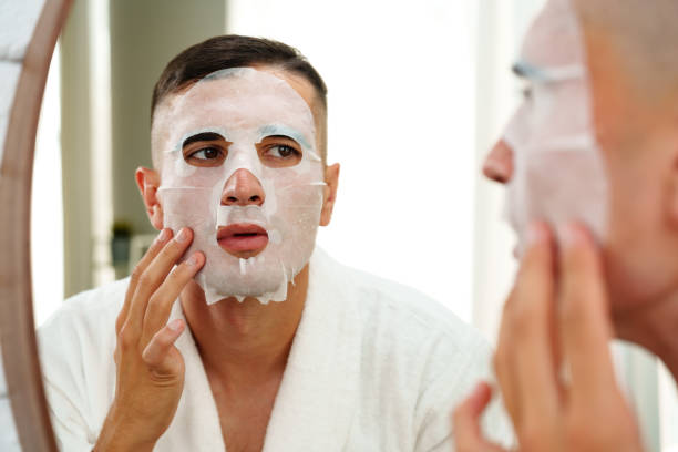 istock Handsome young man applying sheet mask near mirror in bathroom 2180173311