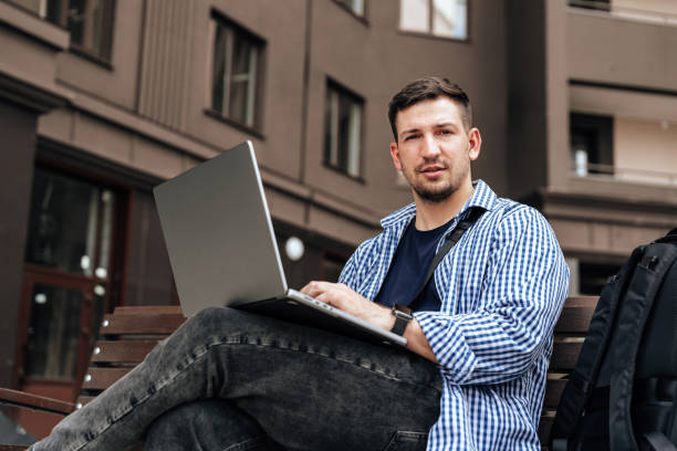 istock Young man working on a laptop while seated on a bench outside 2180179208