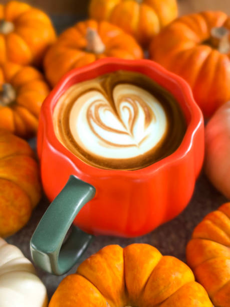 istock Full frame image of orange, pumpkin design coffee mug containing pumpkin spiced latte with milk froth art. flower and leaves design surrounded by mixed munchkin pumpkins and small ornamental gourds, white and orange squashes, elevated view 2180180713
