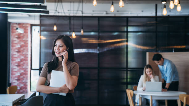 istock A woman is talking on her cell phone while holding a white laptop 2180184198