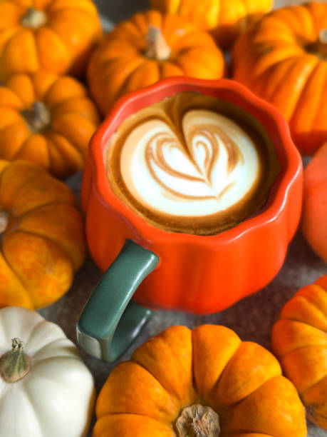 istock Full frame image of orange, pumpkin design coffee mug containing pumpkin spiced latte with milk froth art, flower and leaves design surrounded by mixed munchkin pumpkins and small ornamental gourds, white and orange squashes, elevated view 2180184302