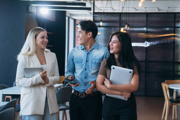 istock Three people are walking together in a room, smiling and holding laptops 2180185551