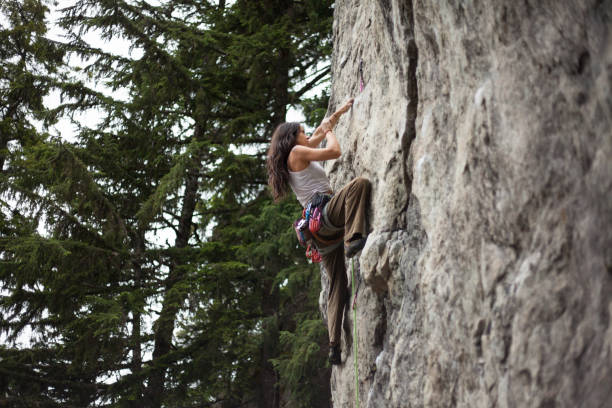Young woman climbs with rope on cliff face in forest