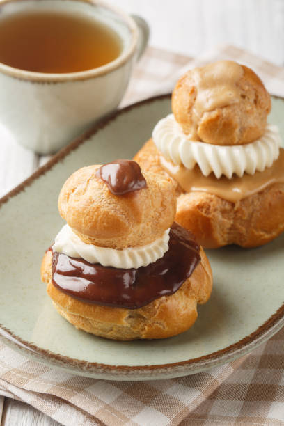 Religieuse choux pastry buns filled with a smooth vanilla pastry cream and coated with dark chocolate ganache or mocha closeup on the plate. Vertical