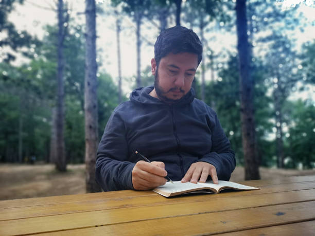 istock Man reading at wooden table in peaceful forest setting 2180194952