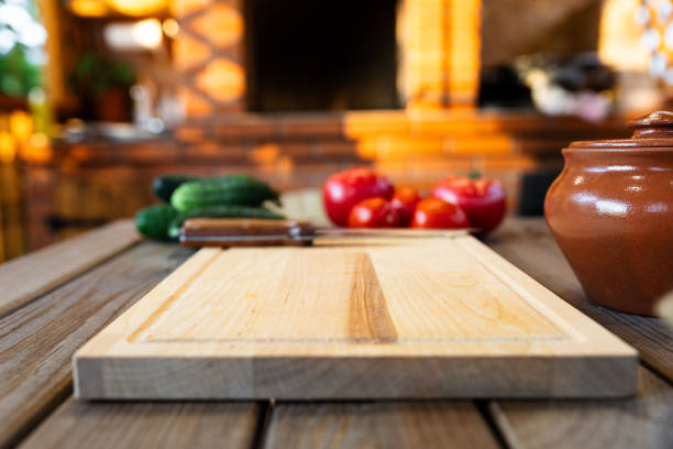 Cutting board on a wooden table, surrounded by fresh vegetables like tomatoes and cucumbers. Rustic kitchen with natural lighting and a brick backdrop.