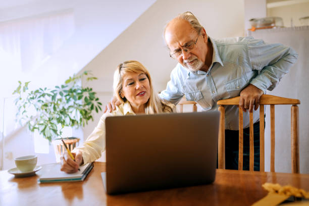 istock Senior man checking on his wife while she is working on laptop at home 2180199606