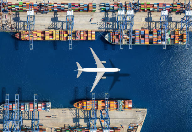 istock Aerial top view of a cargo plane flying above container freight port with docked ships 2180206528