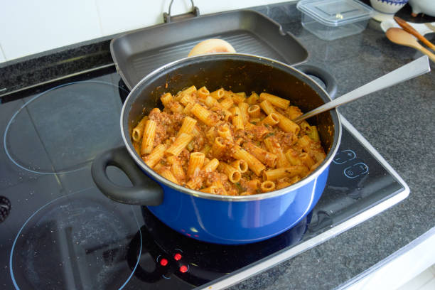 Blue pot with macaroni or rigatoni mixed with bolognese meat sauce on a home electric cooker ready to serve