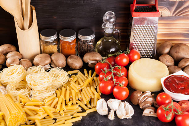 Uncooked raw pasta on rustic background next to variety of vegetables, spices and sunflower oil