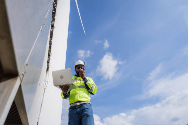 istock A man in a yellow safety vest is talking on a cell phone while looking at a laptop. electrical, engineer, environment, energy, clean, sustainable, wind turbine, nature 2180212674