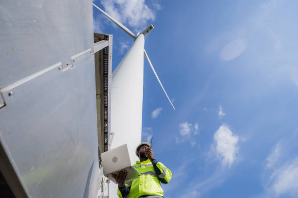 istock A man in a yellow jacket is talking on a cell phone while standing next to a wind turbine. electrical, engineer, environment, energy, clean, sustainable, wind turbine, nature 2180212742
