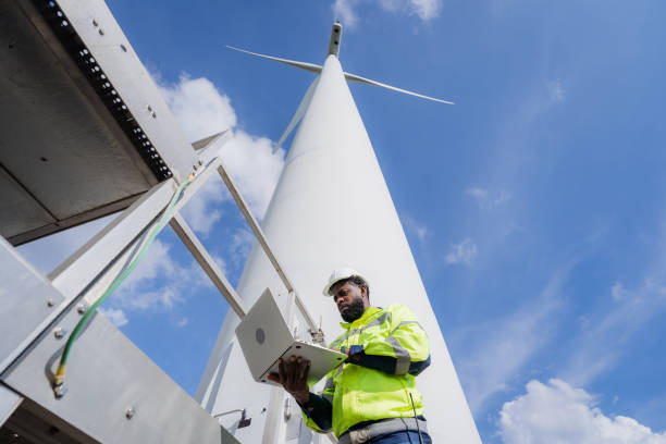 istock A man in a yellow jacket is working on a wind turbine. He is using a laptop to check the turbine's status. electrical, engineer, environment, energy, clean, sustainable, wind turbine, nature 2180212917
