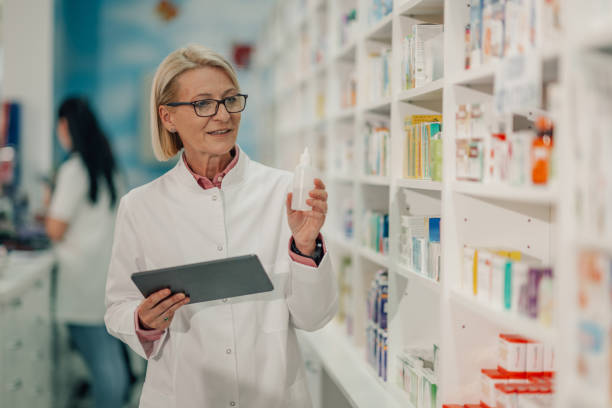 Senior pharmacist using digital tablet checking medicine bottle in pharmacy
