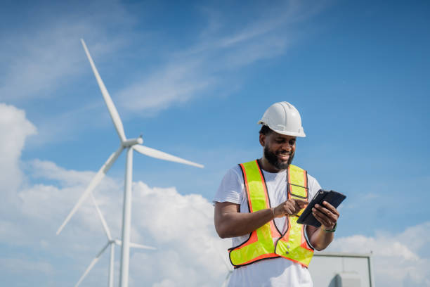 istock A man in a yellow vest is looking at a tablet while standing next to a wind turbine. electrical, engineer, environment, energy, clean, sustainable, wind turbine, nature 2180214043