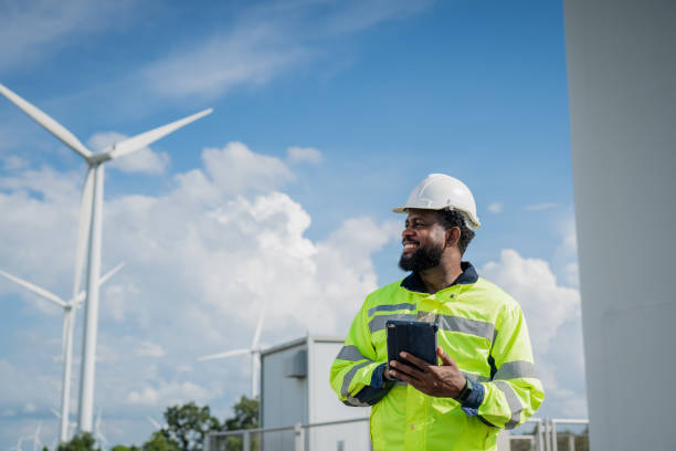 istock A man in a yellow safety jacket is holding a tablet while standing next to a wind turbine. electrical, engineer, environment, energy, clean, sustainable, wind turbine, nature 2180214073
