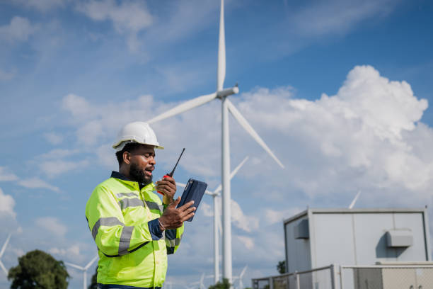 istock A man in a yellow safety vest is talking on a walkie talkie while standing next to a wind turbine. electrical, engineer, environment, energy, clean, sustainable, wind turbine, nature 2180216202