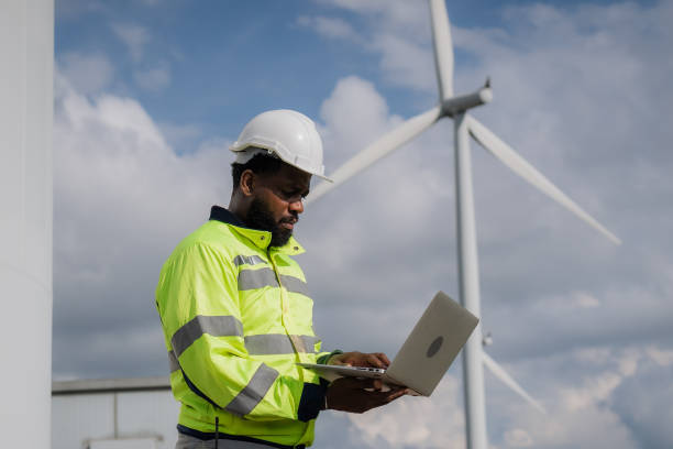 istock A man in a yellow and black safety vest is using a laptop computer. He is wearing a hard hat and safety glasses. electrical, engineer, environment, energy, clean, sustainable, wind turbine, nature 2180217514