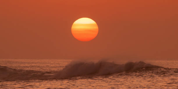 Beautiful sunset over the ocean with a glowing sun and soft waves, creating a peaceful and tranquil scene. Perfect for concepts of relaxation, nature, and calm atmospheres. Ideal for backgrounds.
