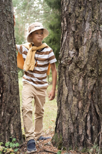 istock A little boy on a walk in the forest or park, peeking out from behind a tree. 2180223245