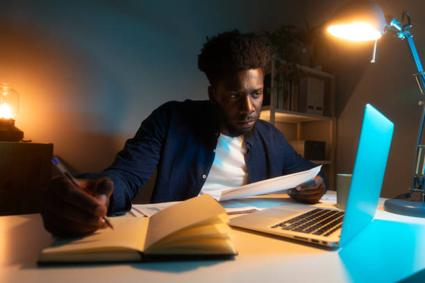 istock Young African American man studying late at night at home. Black man working using laptop. 2180228657