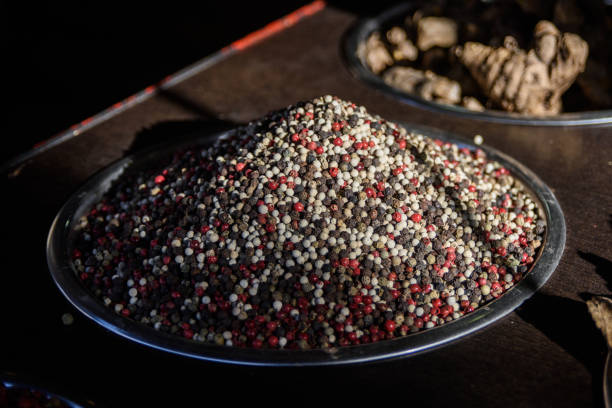 Large silver bowl filled with fresh, whole red, black and white peppercorns piled high and bathed in sunlight.
