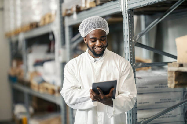 istock Black storage manager in sterile uniform working on checklist and smiling at tablet at warehouse. 2180231003