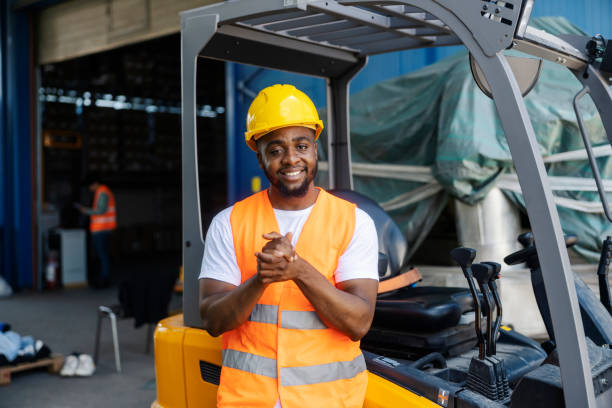 istock Smiling diverse forklift driver in protective uniform smiling at camera at industrial zone. 2180231411