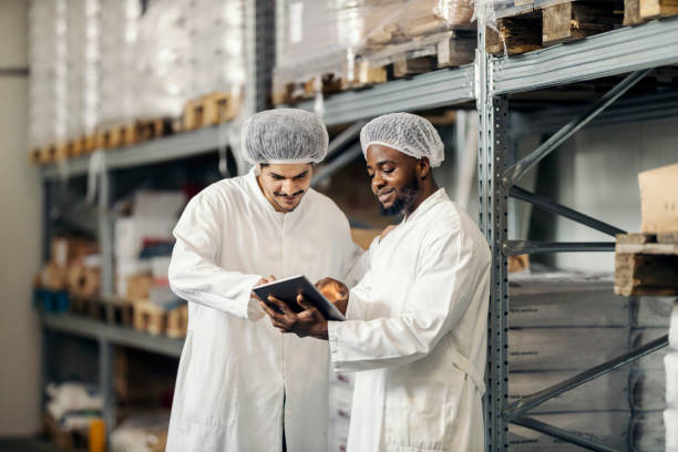istock Multicultural warehouse workers in uniforms scrolling on tablet and adding supplies on it at storage 2180231543
