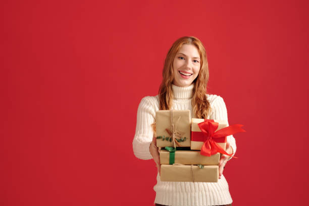 istock Smiling Woman Holding Gift Boxes on Red Background 2180236145