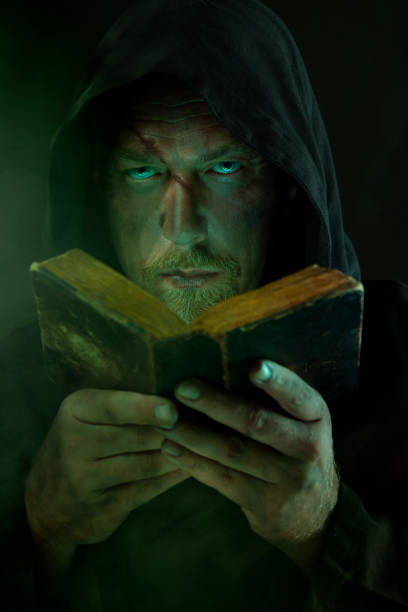 Hooded man intently reading an old, worn book in a dark, mysterious setting with green lighting, evoking mystery and intrigue.
