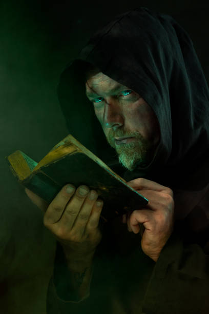 istock Hooded Man Reading Ancient Book in Dark 2180237428