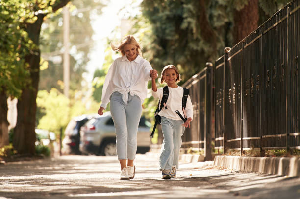 istock Front view, walking. Schoolgirl with her mother are outdoors together 2180243009