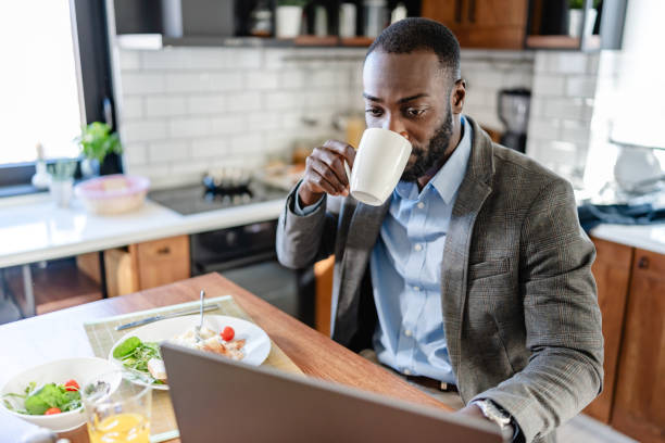 istock African-American man in a modern kitchen, drinking coffee and working on a laptop during breakfast. Bright and productive morning scene. 2180245335