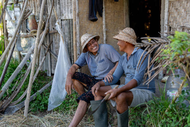 Happy Asian farmers laughing while taking a break from harvesting the land in Bali and sitting outside a hut
